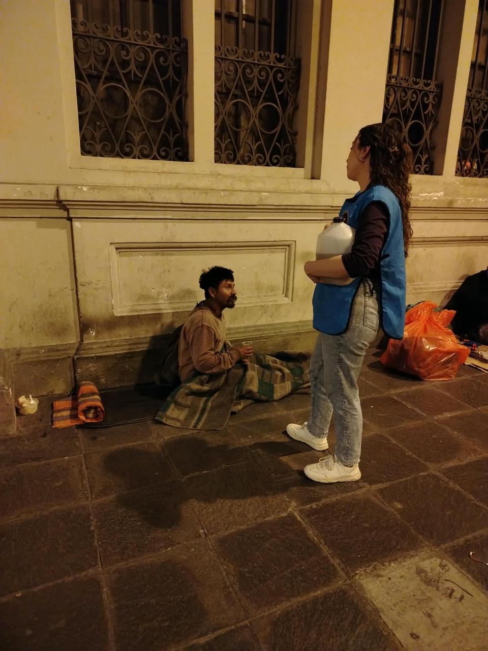 Una voluntaria conversa con un hombre sentado sobre una manta en la vereda