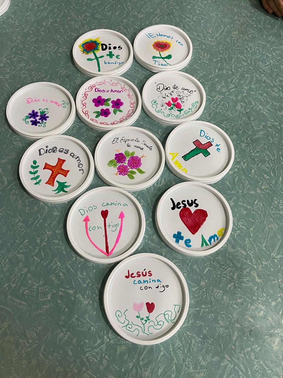Tapas blancas decoradas a mano con flores, corazones y mensajes como «Dios es amor»