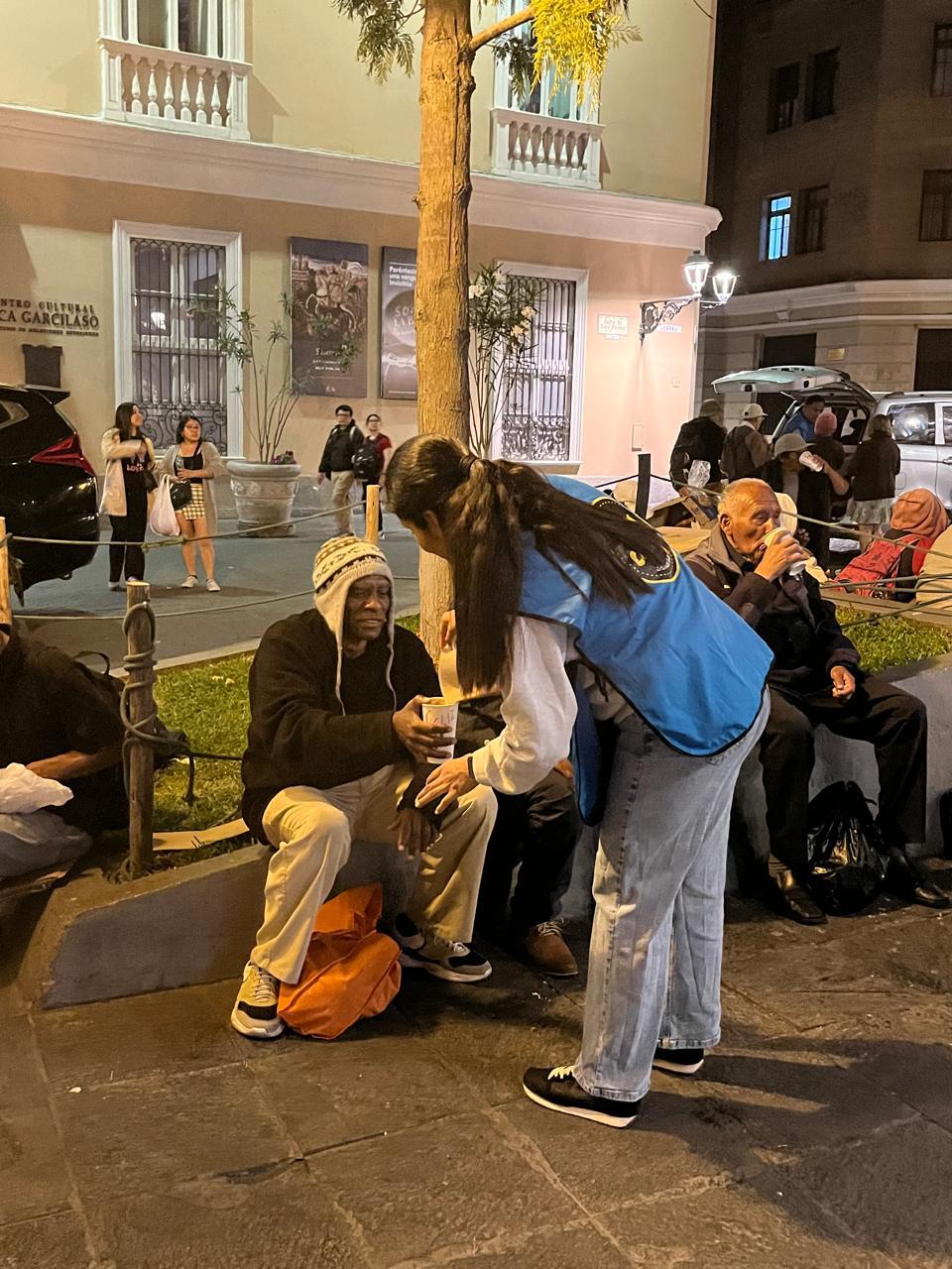 Una voluntaria entrega un vaso a un hombre sentado en una plaza