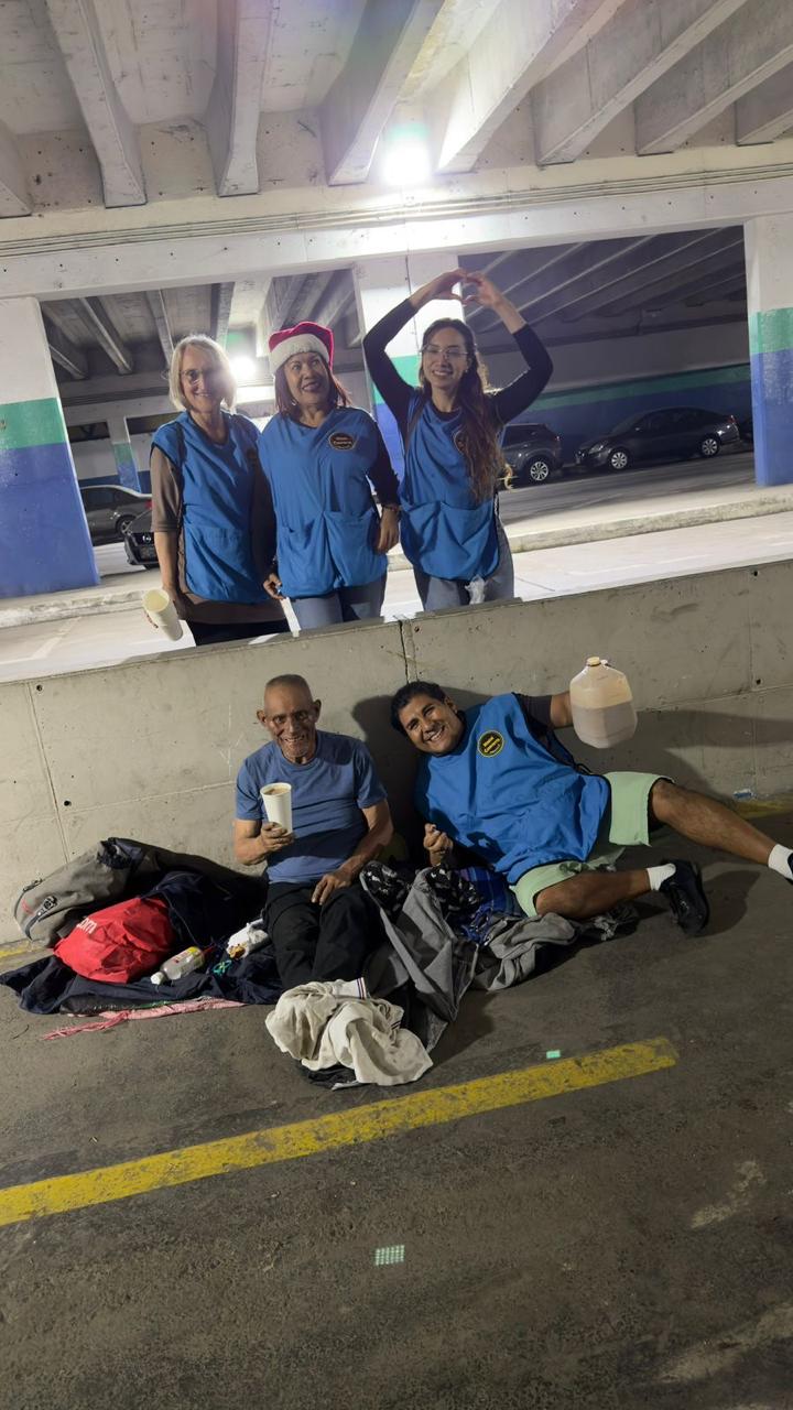 Voluntarios sonríen junto a dos personas a las que acaban de servir comida y bebida