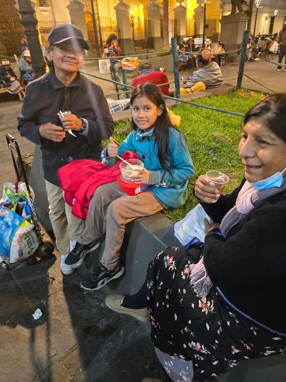 Tres personas sonríen en una plaza mientras comen la comida que recibieron de Misión Compartir